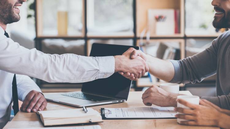 Sealing a deal. Side view close-up of two young man shaking hands while sitting at the wooden desk